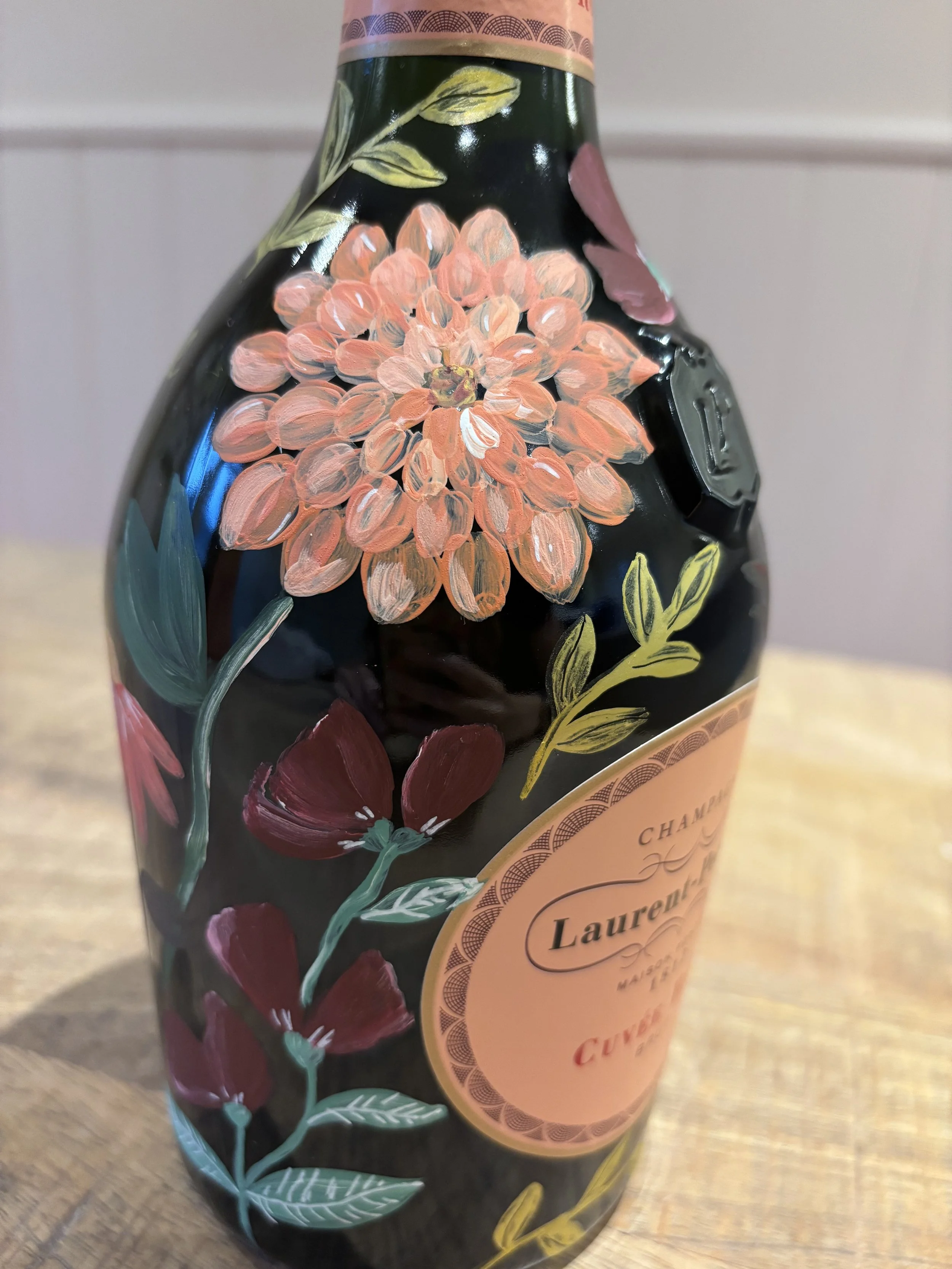 Hand painted bottle of champagne painted with pink flowers and orange flowers.