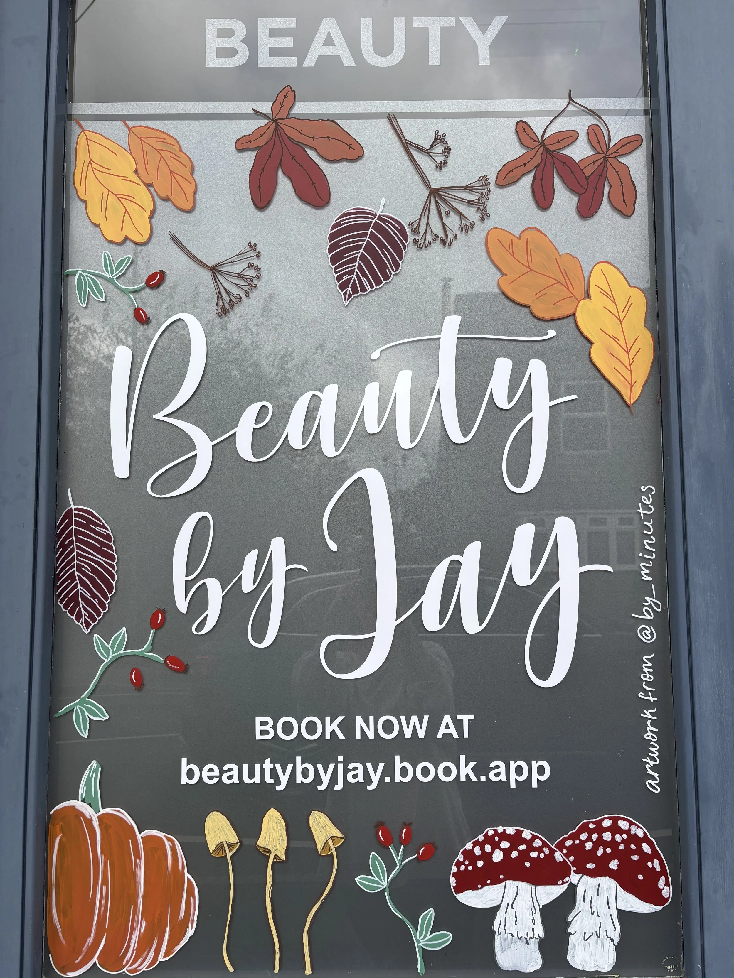 Decorative window sign for 'Beauty by Jay' with autumn-themed illustrations including leaves, berries, pumpkins, mushrooms, and acorns.