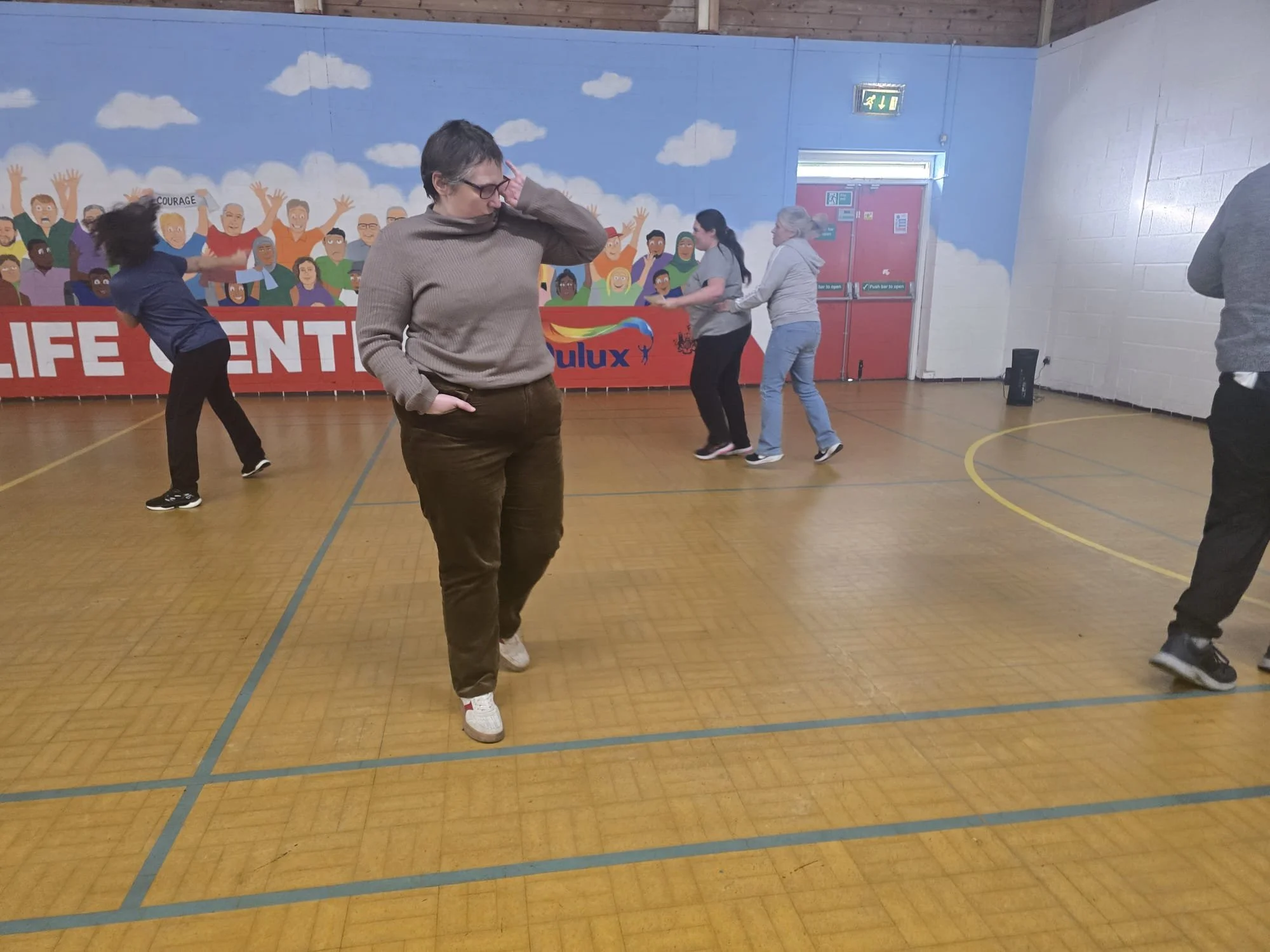 People dancing in a gymnasium with mural art and a Dulux banner on the wall.