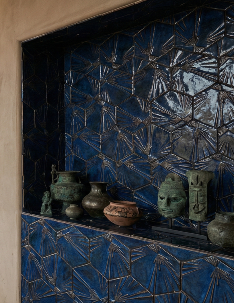 Blue tiled wall with geometric patterns and a shelf holding various antique ceramic and bronze artifacts including vases and sculptures.