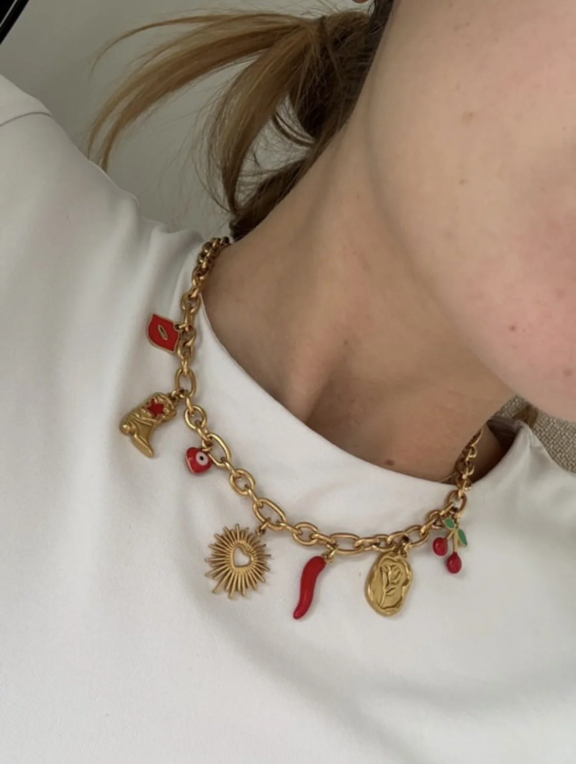Collier en or avec divers pendentifs colorés, dont une étoile, un visage, un chili, un cœur, un œil, une cerise et une feuille sur un fond blanc
