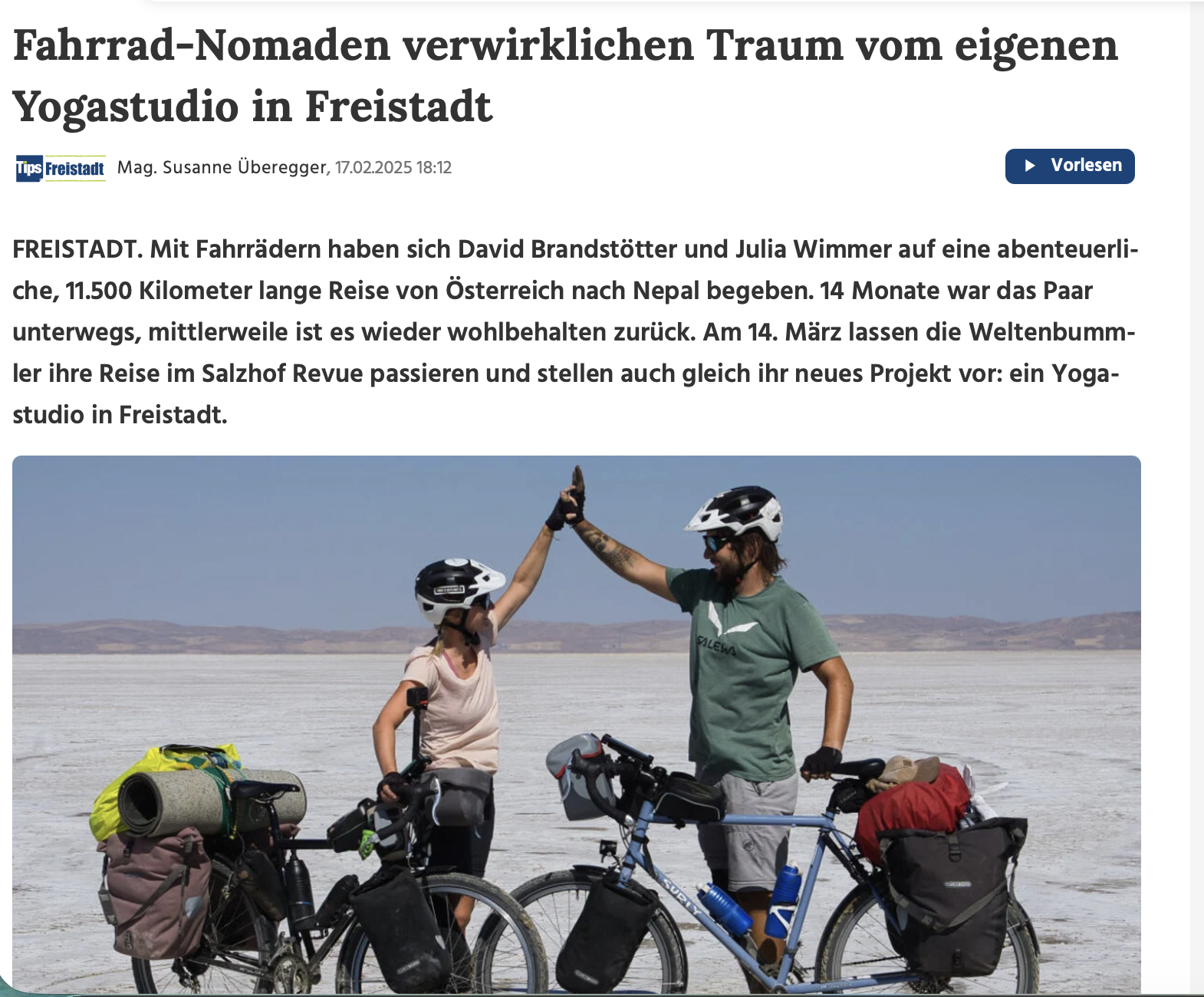 Two cyclists, a man and a woman, wearing helmets, giving each other a high five in a flat, open landscape with backpacks and gear on their bikes.