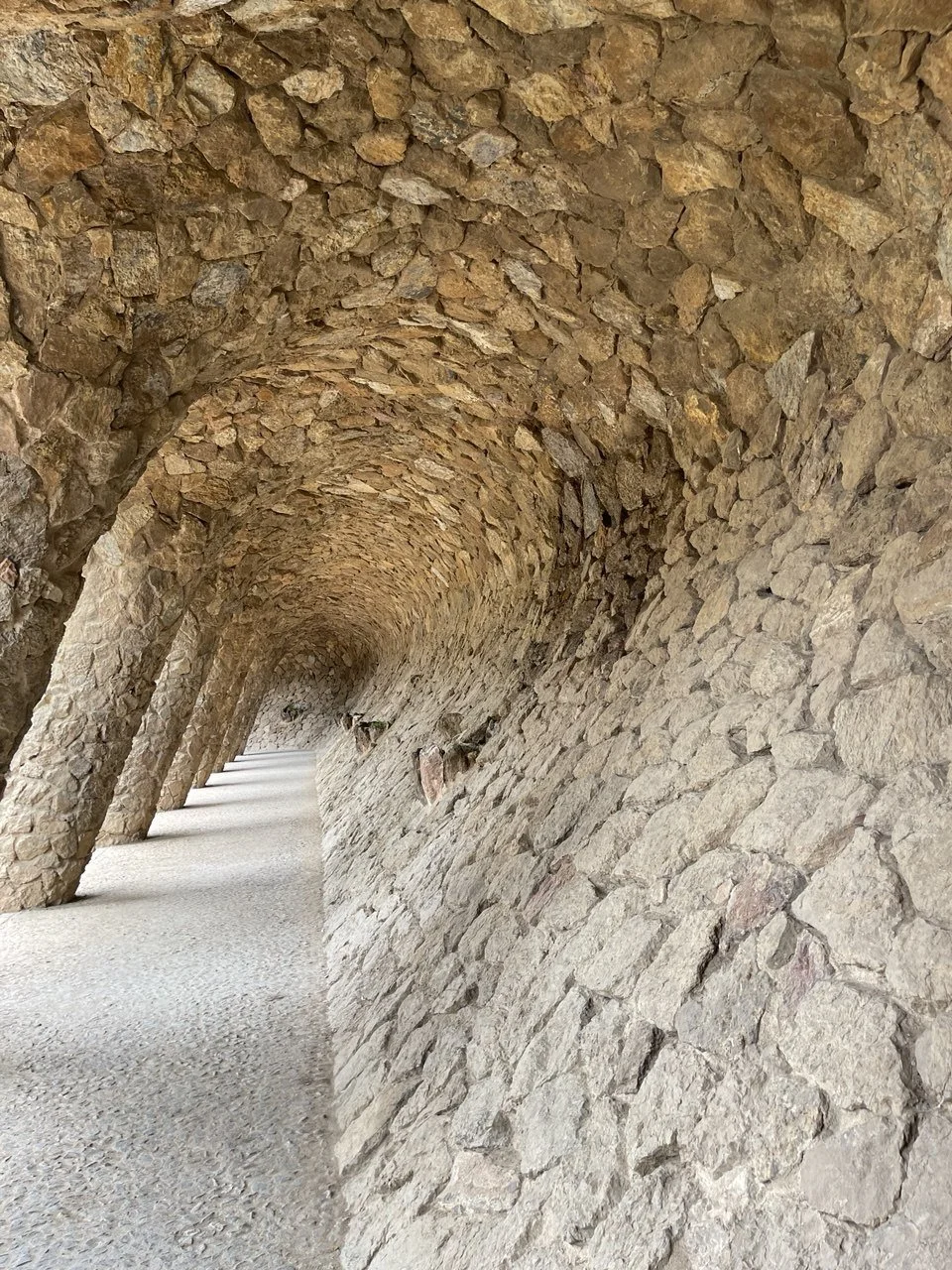 Stone arch tunnel with rough-hewn stone walls and ceiling, and a gravel pathway inside.