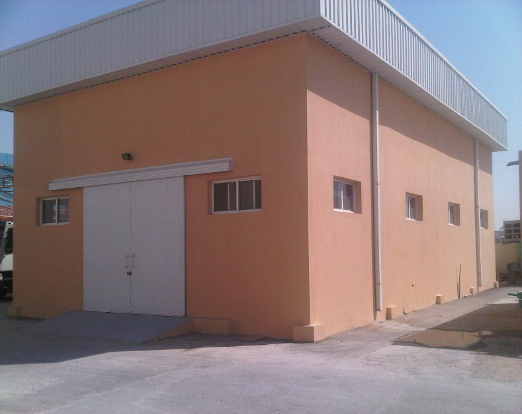 A peach-colored commercial building with a white metal roof and a large white door, with small windows on the side.