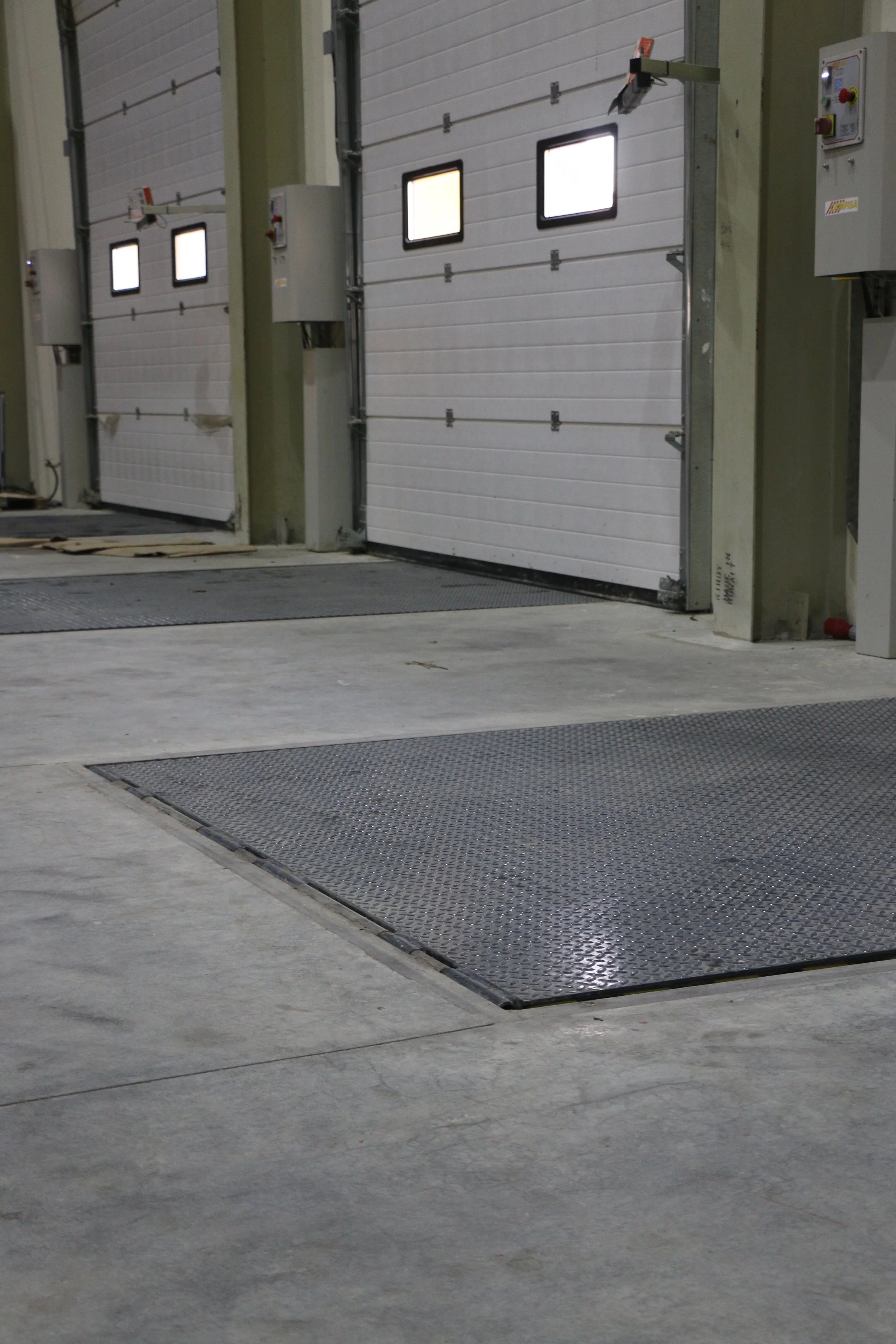 Indoor industrial garage with three large white rolling doors and metal ramps on the concrete floor.