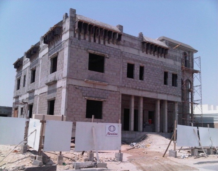Under-construction multi-story building made of gray bricks, with scaffolding on the side and construction barriers in the foreground.