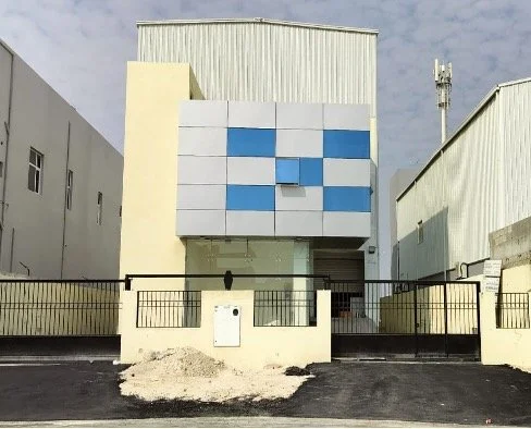 Modern building with blue and white checkered facade, front gate, and small yard in an industrial area.