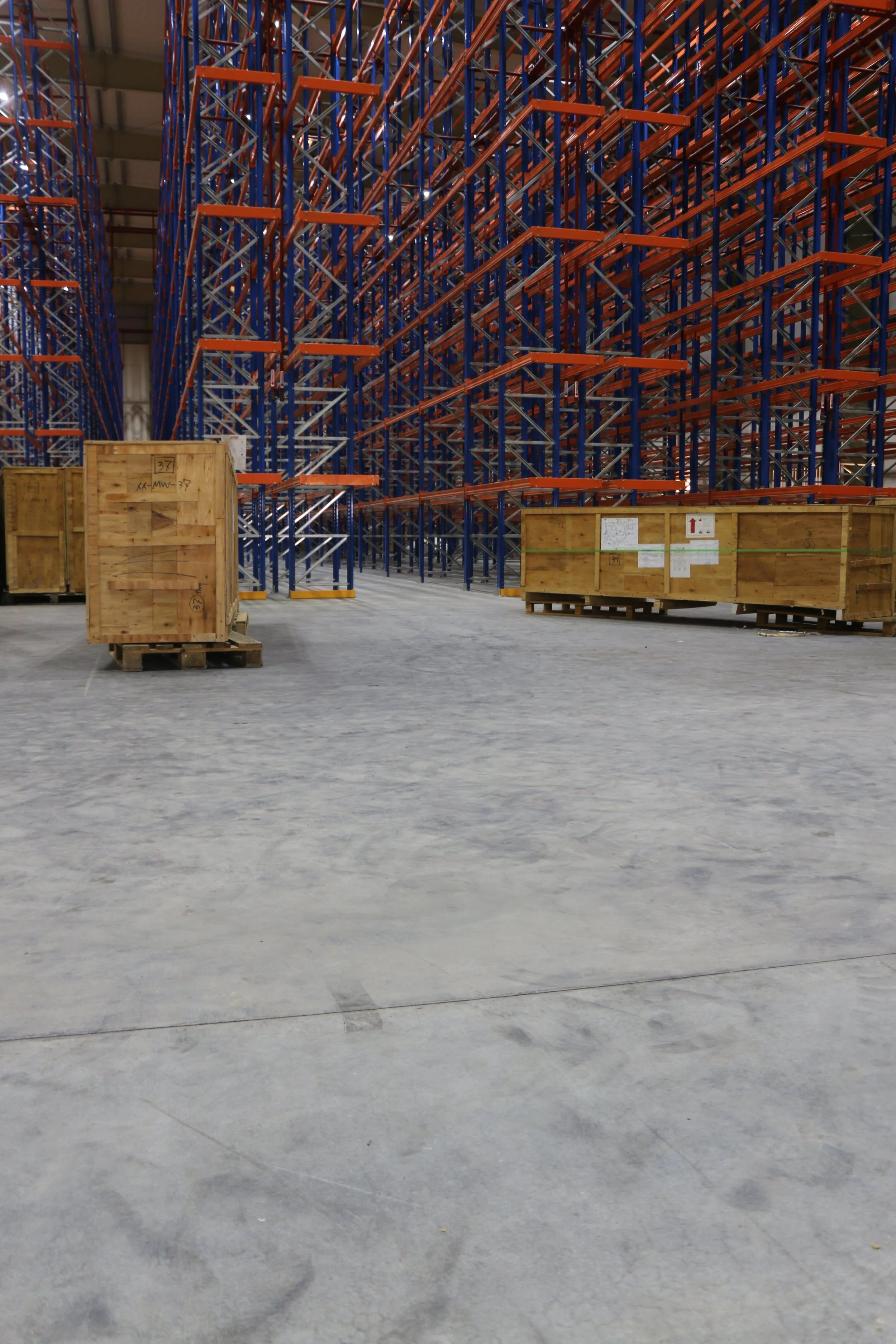 Empty warehouse with tall blue and orange storage racks and wooden crates on pallets.
