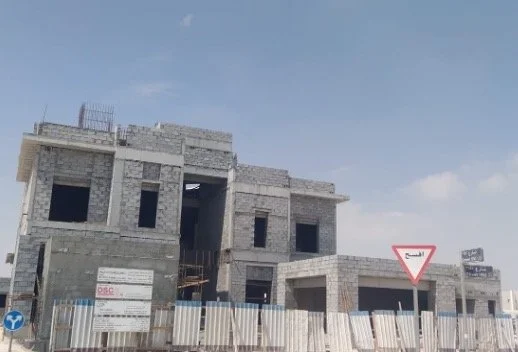 Construction site with a partially built multi-story concrete building, safety signs, and a clear blue sky.