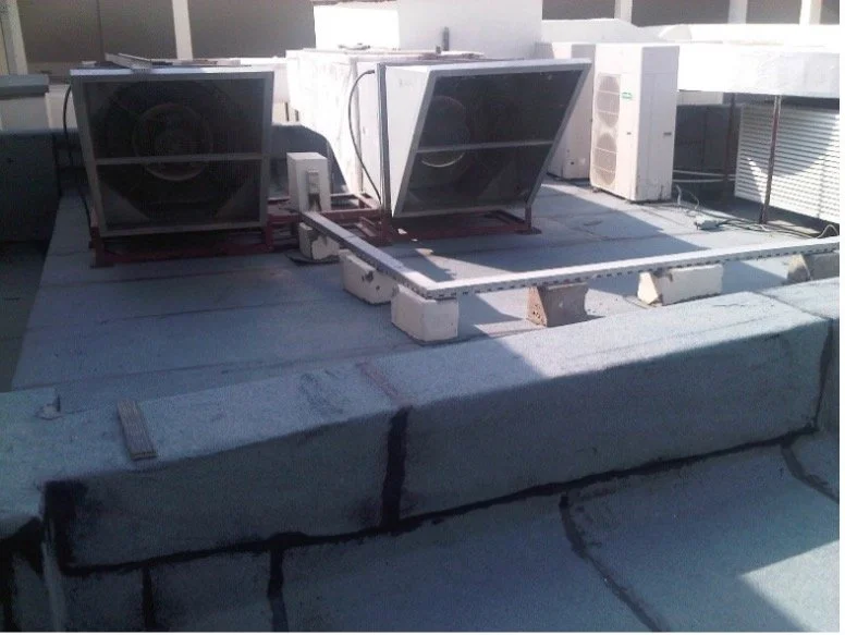 Rooftop air conditioning units installed on a building roof with concrete blocks and safety barrier.