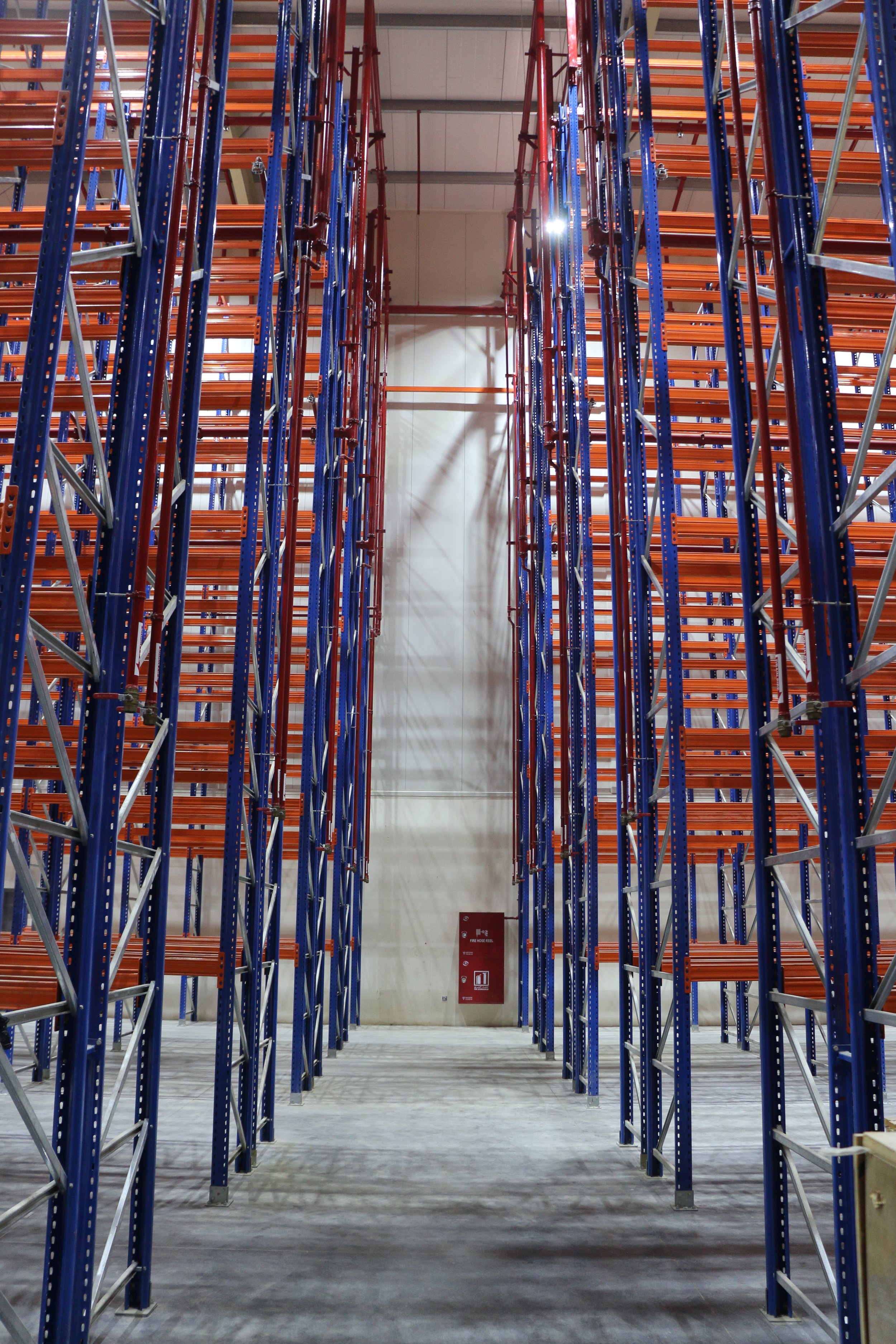 Empty warehouse storage racks with orange shelves and blue metal frames, taken from the ground looking up.