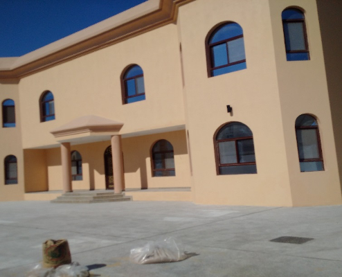 Front view of a tan building with arched windows and a set of stairs leading to the entrance.