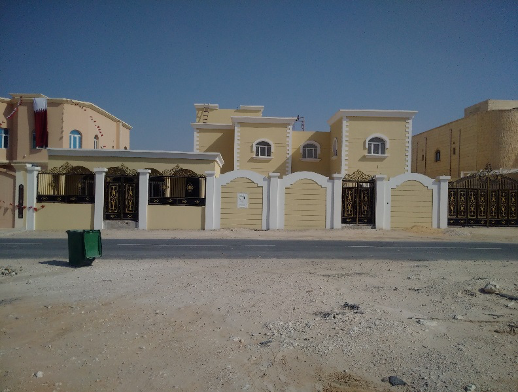 Residential houses with beige walls and white accents, black and gold gates, and a clear blue sky.