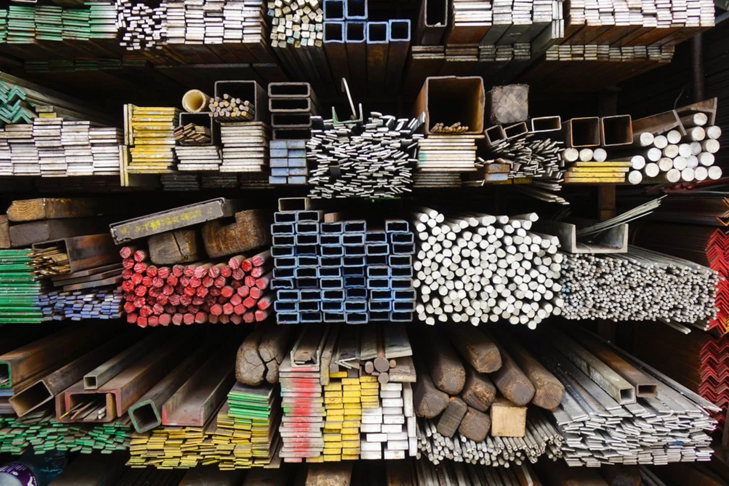 A top-down view of a store shelf stocked with various metal pipes and rods of different sizes, shapes, and colors, arranged in organized stacks.