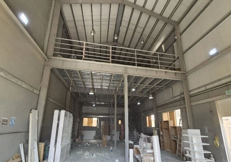 Interior of an industrial building under construction with finished metal walls and ceiling, metal staircase, and various construction materials and tools scattered on the floor.