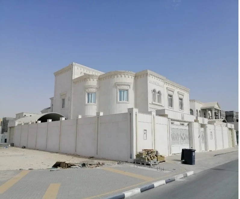 A large white mansion with a high wall surrounding it, under a clear blue sky.
