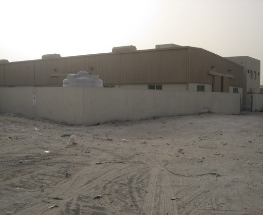 Industrial building with beige walls and a concrete barrier in a desert area with sandy ground.