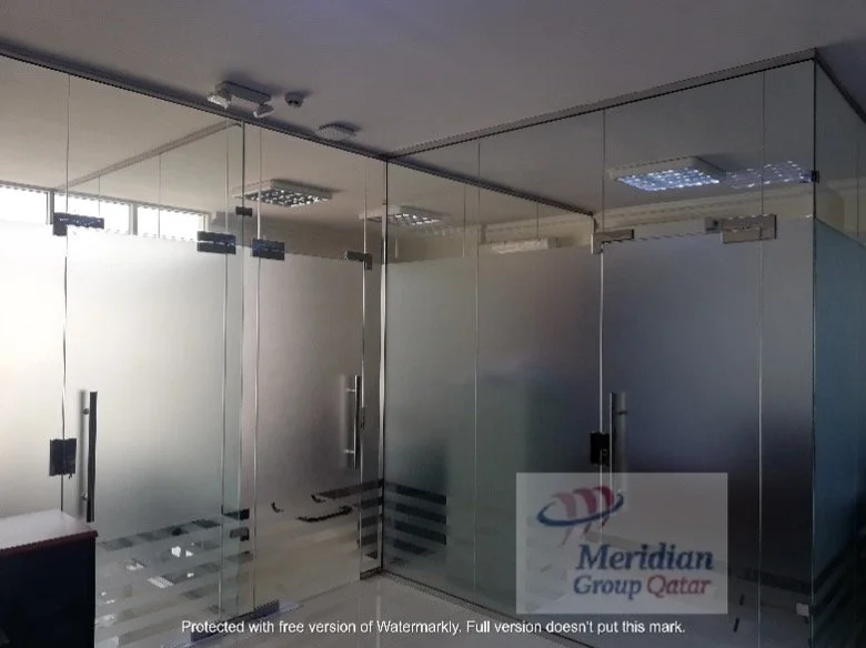 A young man sitting on a beige cushioned bench in a neutral-colored room, wearing a gray polo shirt and cream-colored pants, with a serious expression and shadow cast on the wall behind him.