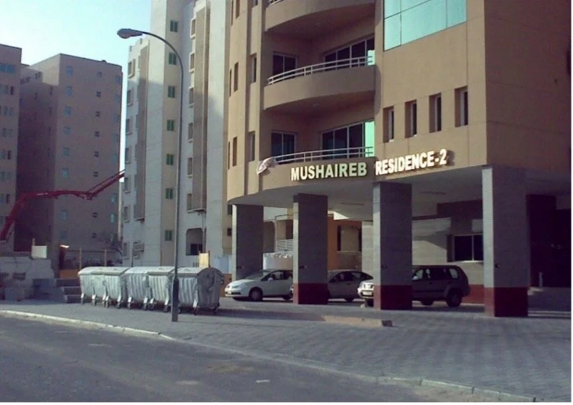 Apartment building with a sign labeled "Mushairab Residence-2" and parked cars in front.