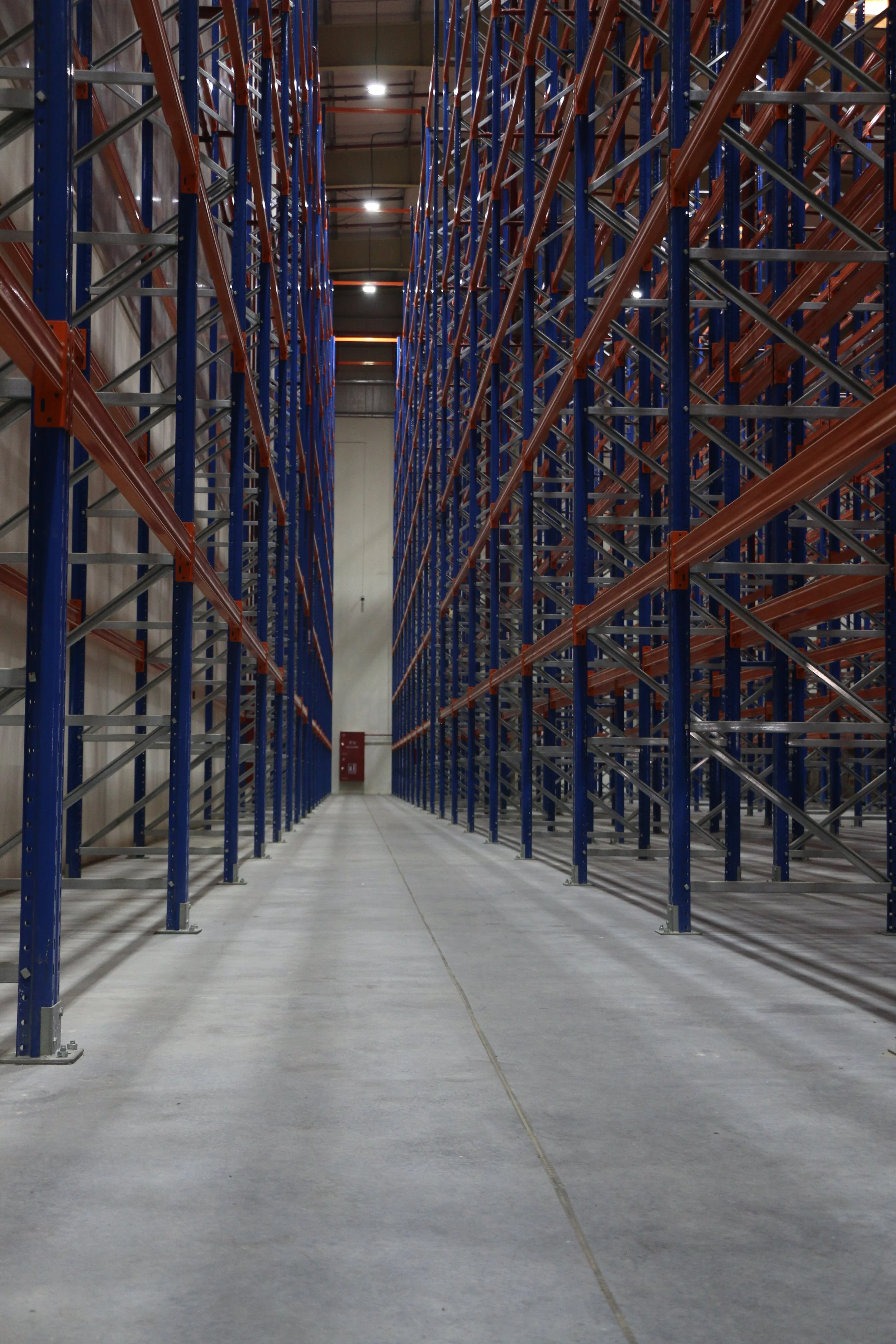 Empty warehouse aisles with tall blue and orange metal storage racks.