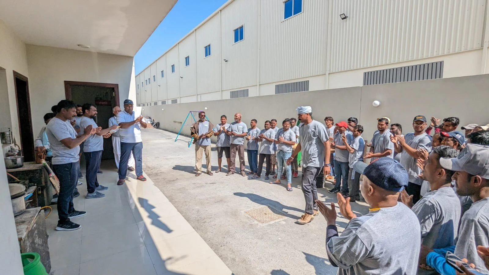 Meridian Team standing outdoors near a building, participating in a gathering or celebration, some are clapping and some are taking photos.