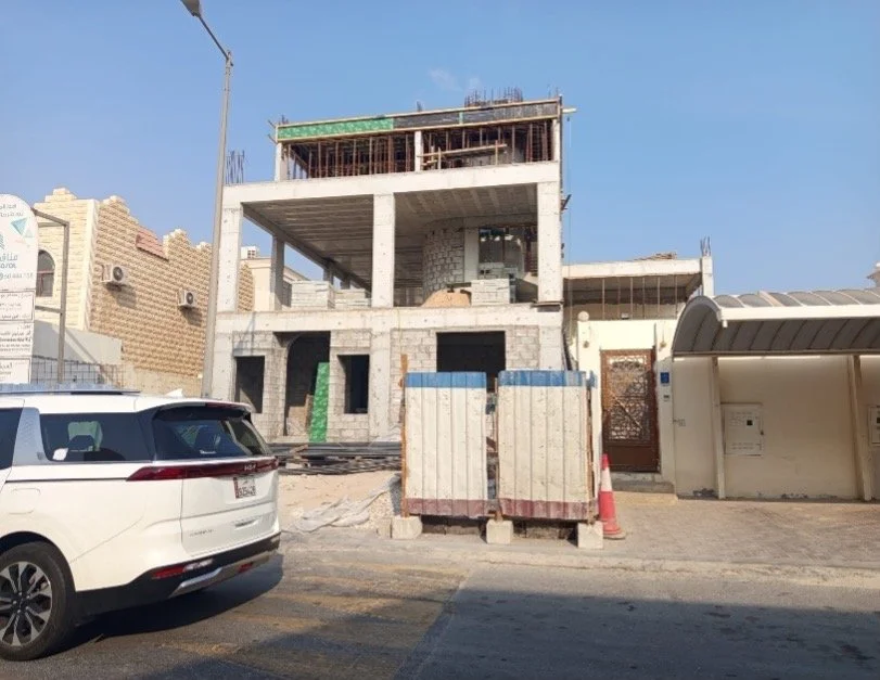 Under construction multi-story building on a city street with parked car, construction barriers, and a bus stop shelter