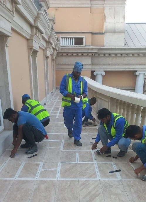 Several workers in safety vests installing or repairing floor tiles on a balcony or terrace.