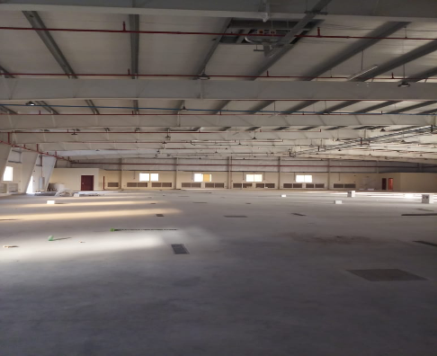 Empty indoor construction site with unfinished concrete floor and ceiling, orange pipes, and windows along the back wall.