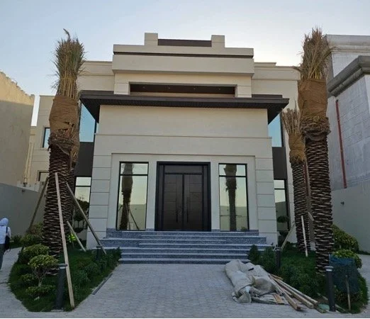 Front view of a modern, multi-story house with palm trees on either side and steps leading to the entrance.