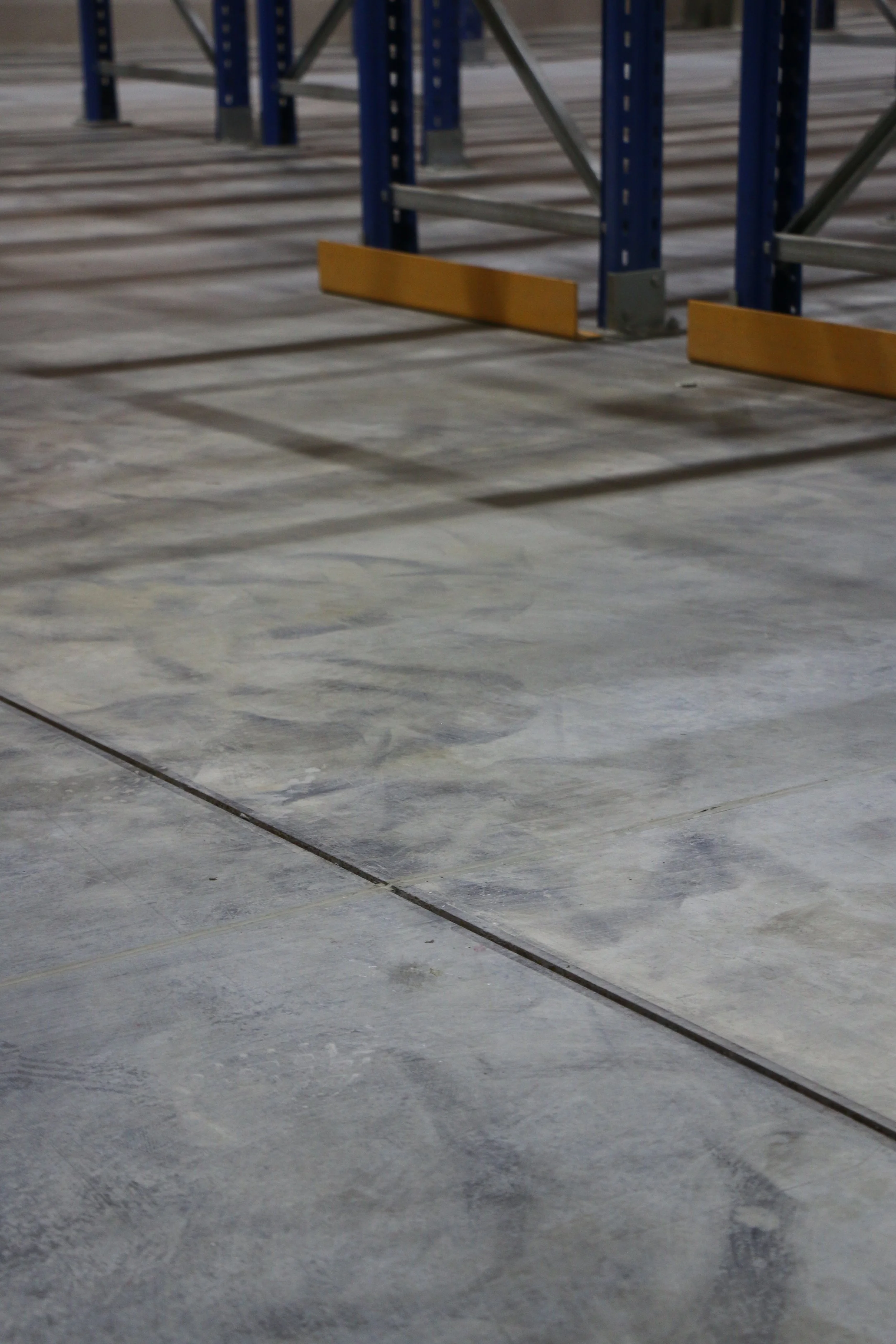 Empty warehouse with concrete floor, metal shelving units, and yellow safety barriers.