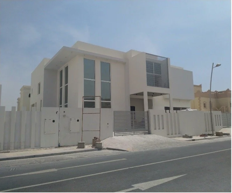 Modern white house with large windows and a gated fence on a street with a sidewalk and streetlight.
