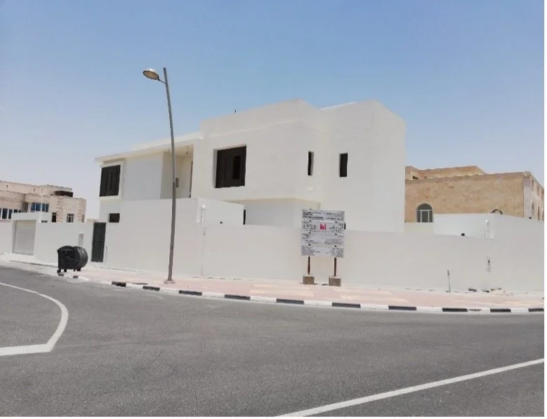 Modern white residential building on a curved street with a streetlamp, trash bin, and a sign in front, under a clear sky.