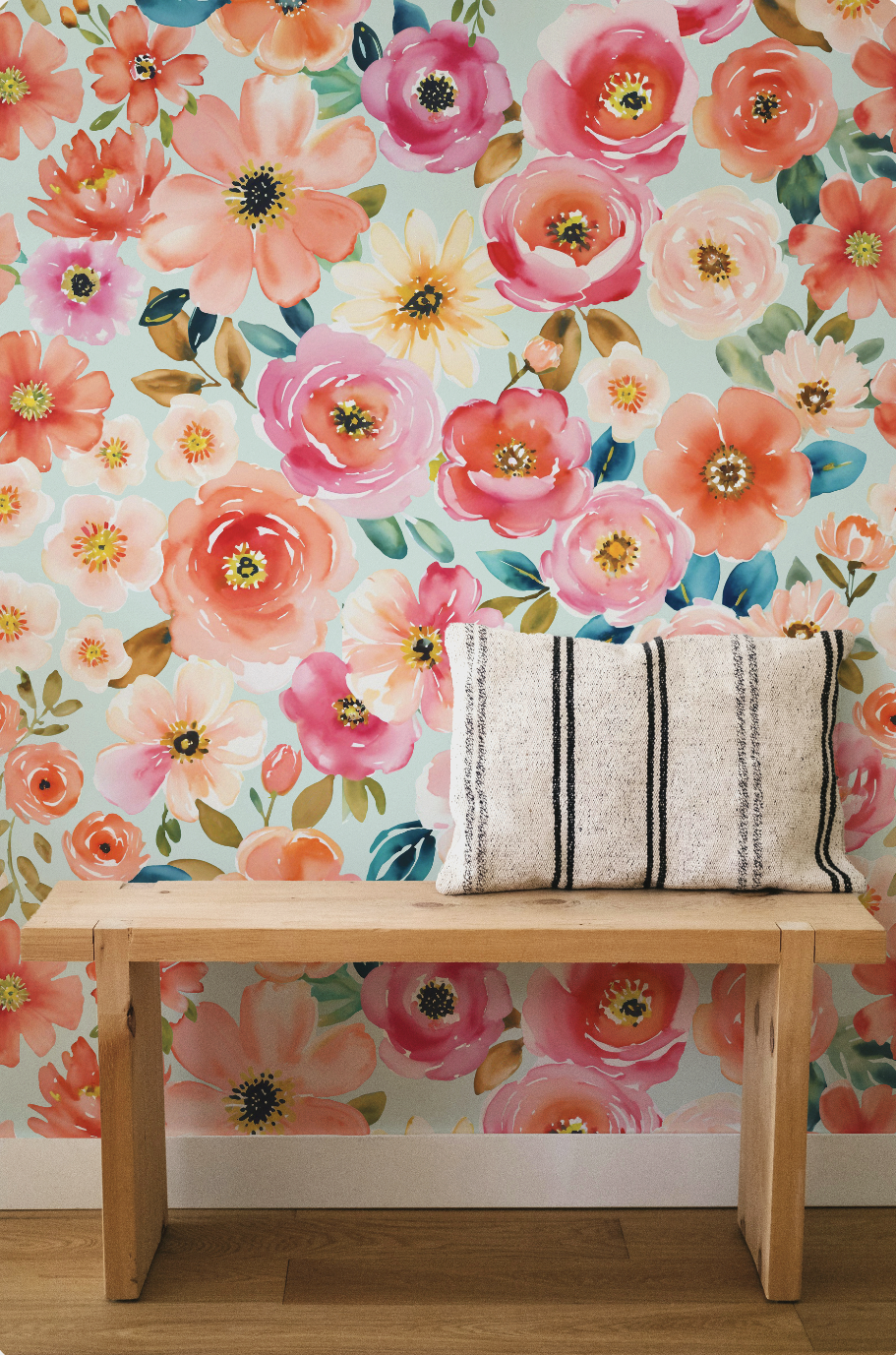 A wooden bench with a striped pillow against a floral wallpaper with large pink, peach, and yellow flowers on a light blue background.