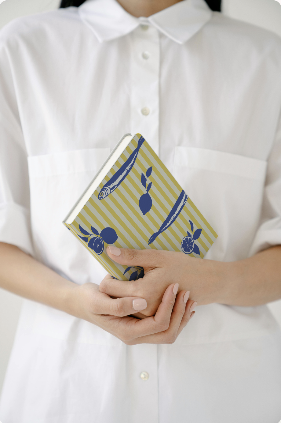 Person in a white shirt holding a patterned notebook with illustrations of fish, lemons, and oranges.