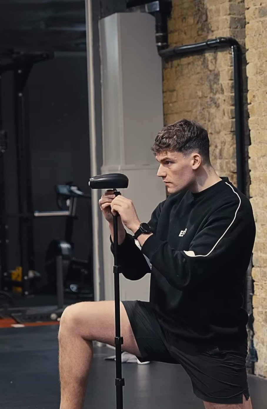 A young strength and conditioning coach adjusting a speed gate at the gym, holding a weight plate with a resistance machine in the background. Athletic performance expert