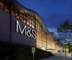 The exterior of an M&S store at night with illuminated signage and modern architecture.