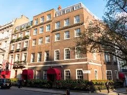 A multi-story brick building with several windows and red awnings, situated on a city street with trees and pedestrians.