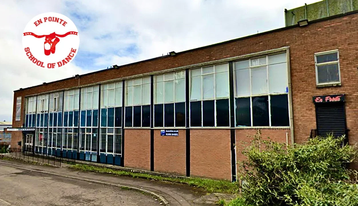 Exterior of a brick building with large glass windows and a sign indicating it is a dance school, with the schools logo of in the top left corner reading 'En Pointe School of Dance'.
