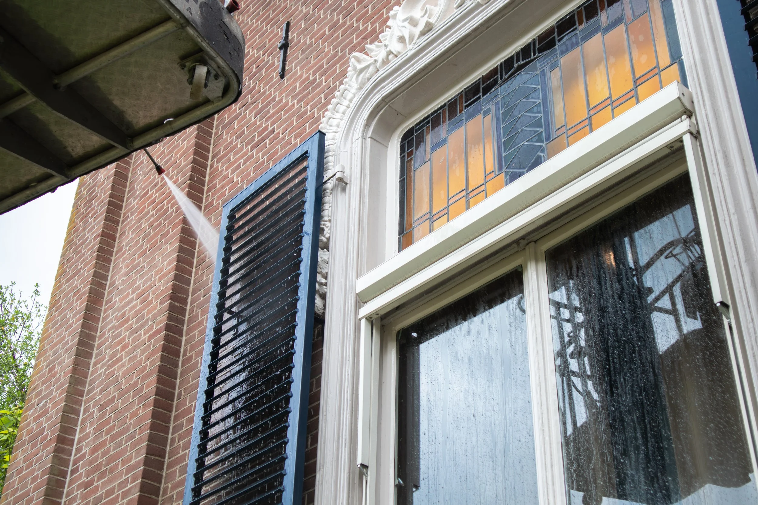 Een close-up van een raam met een zwarte luiken, een raam open en afwasmiddel wordt op het venster gedoucht, een gevel van bakstenen en een lantaarnpaal op de achtergrond.
