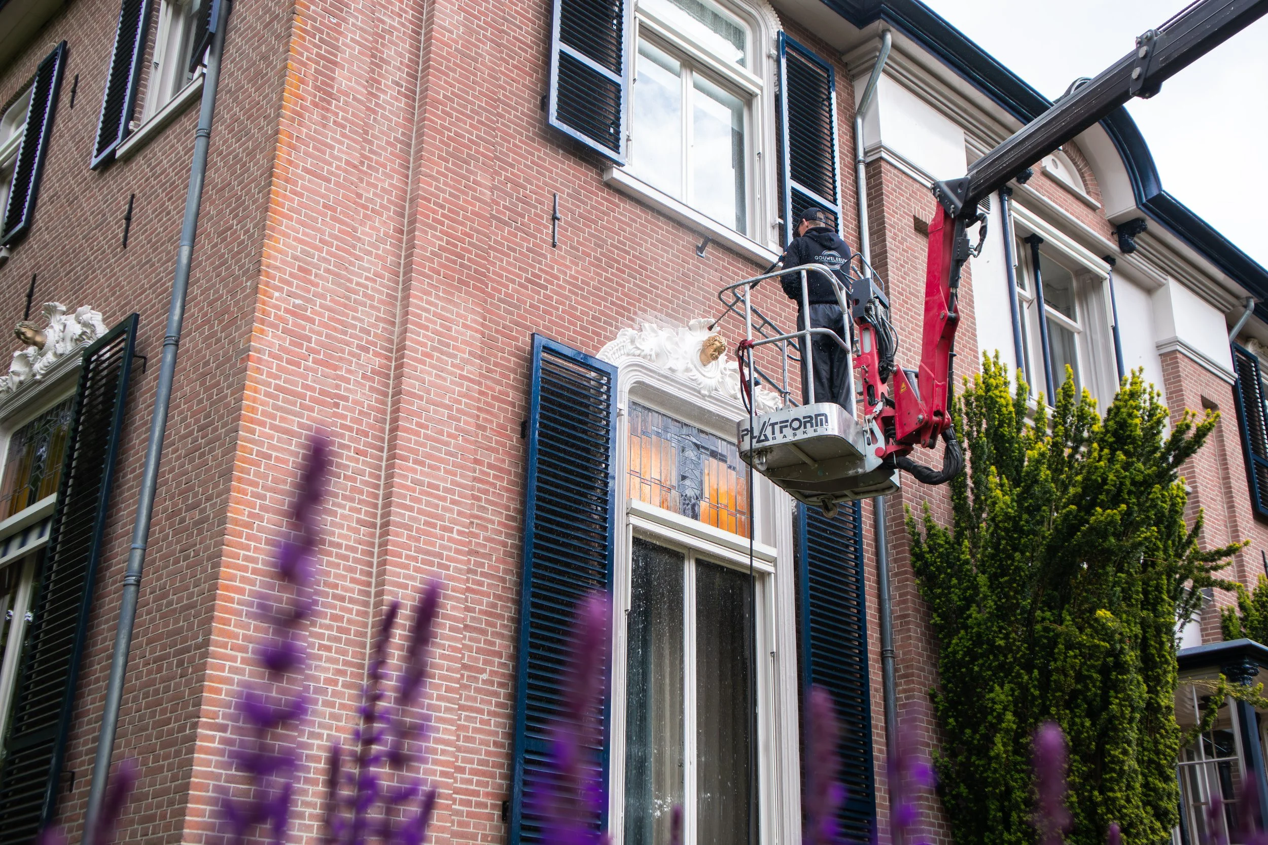 Een bouwvakker op een hoogwerker die een raam van een bakstenen gebouw schoonmaakt of repareert.