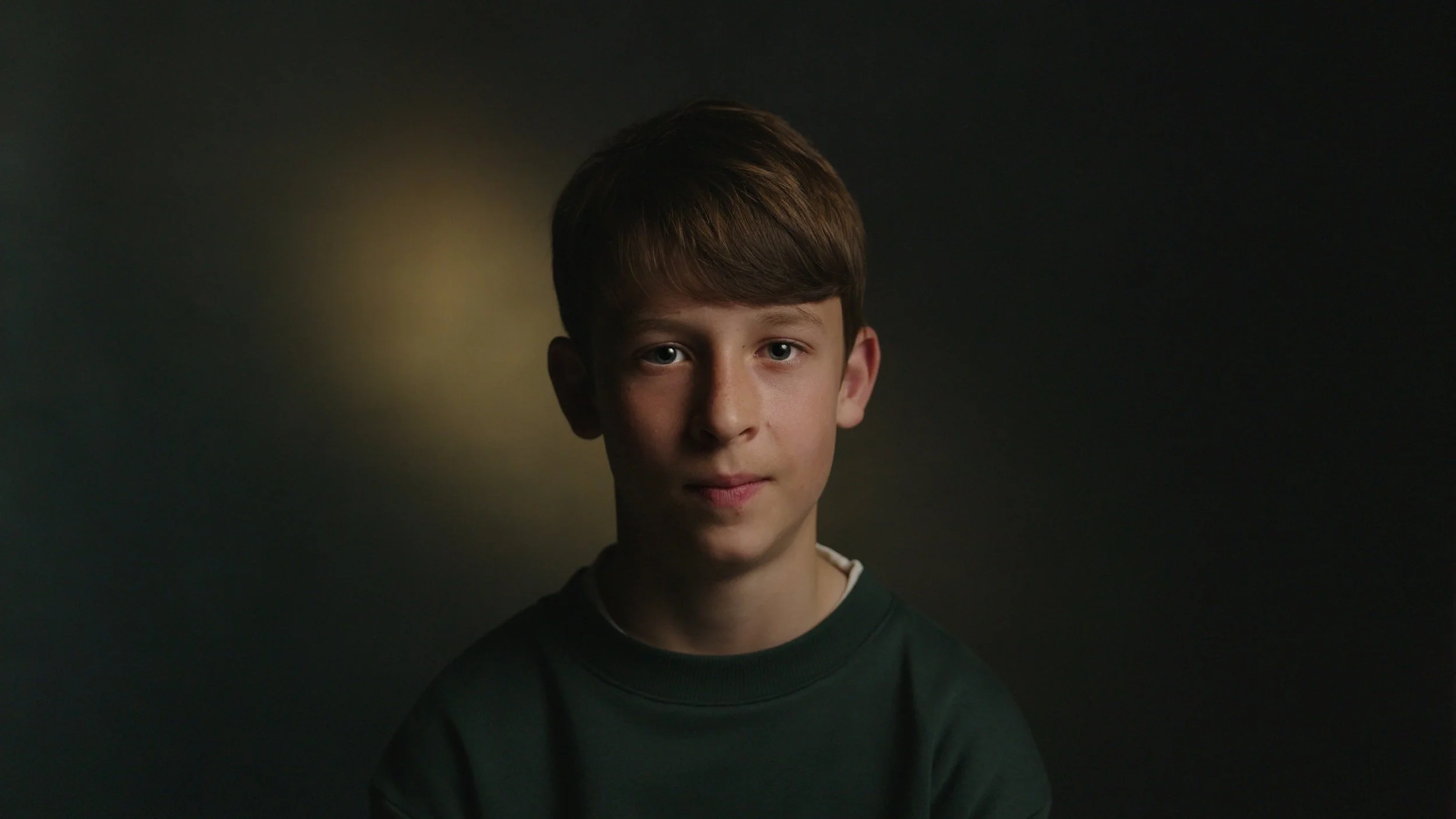 A young boy is interviewed in a dark setting with moody lighting