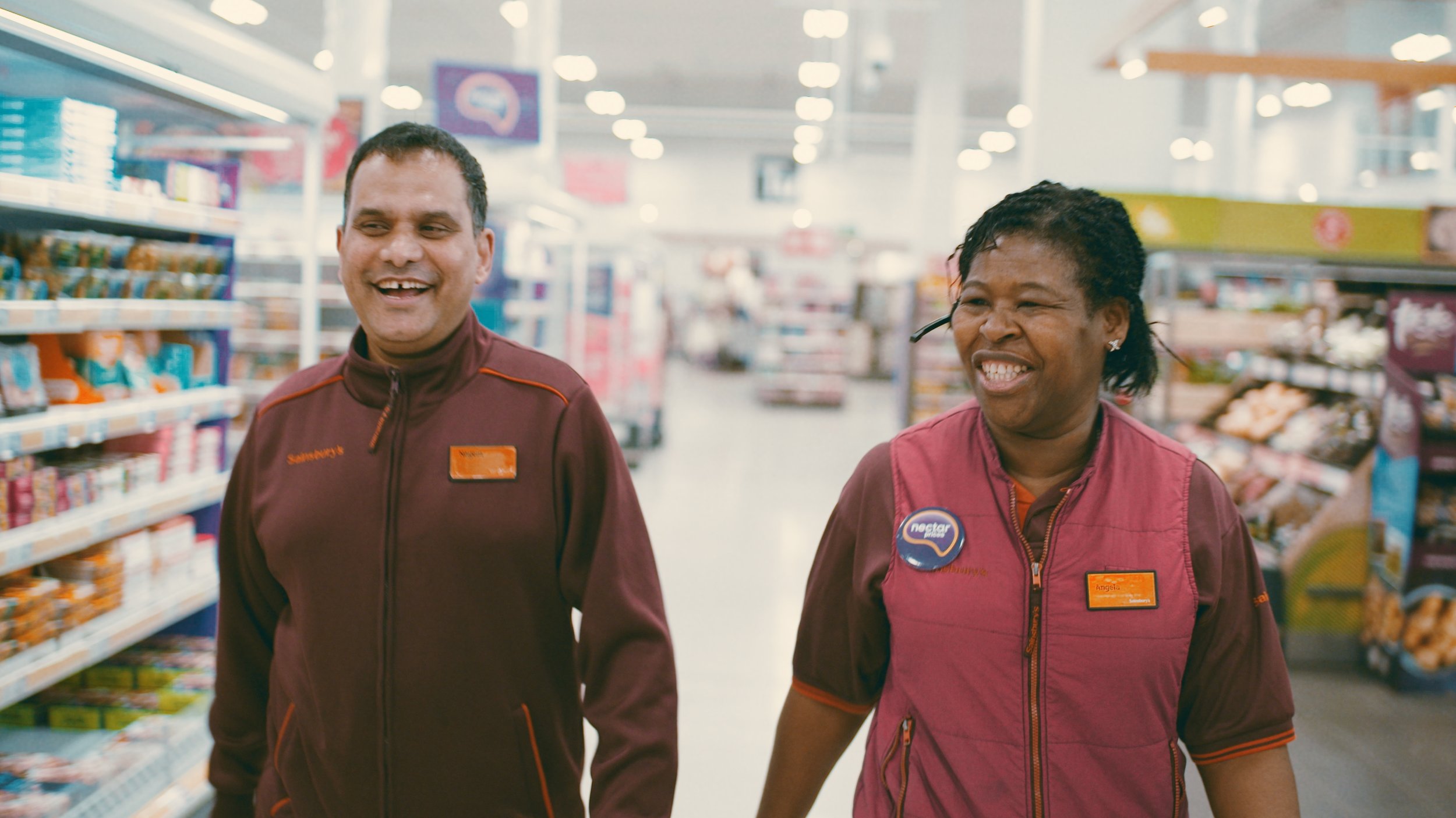 Two Sainsburys workers smile as they walk through the store