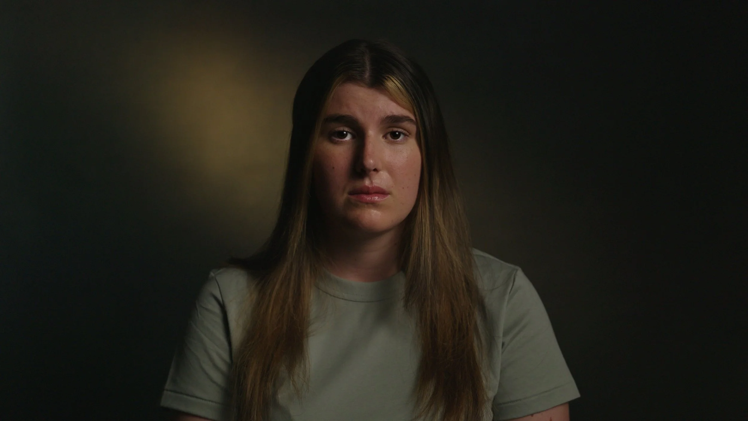 A woman  is interviewed in a dark setting with moody lighting