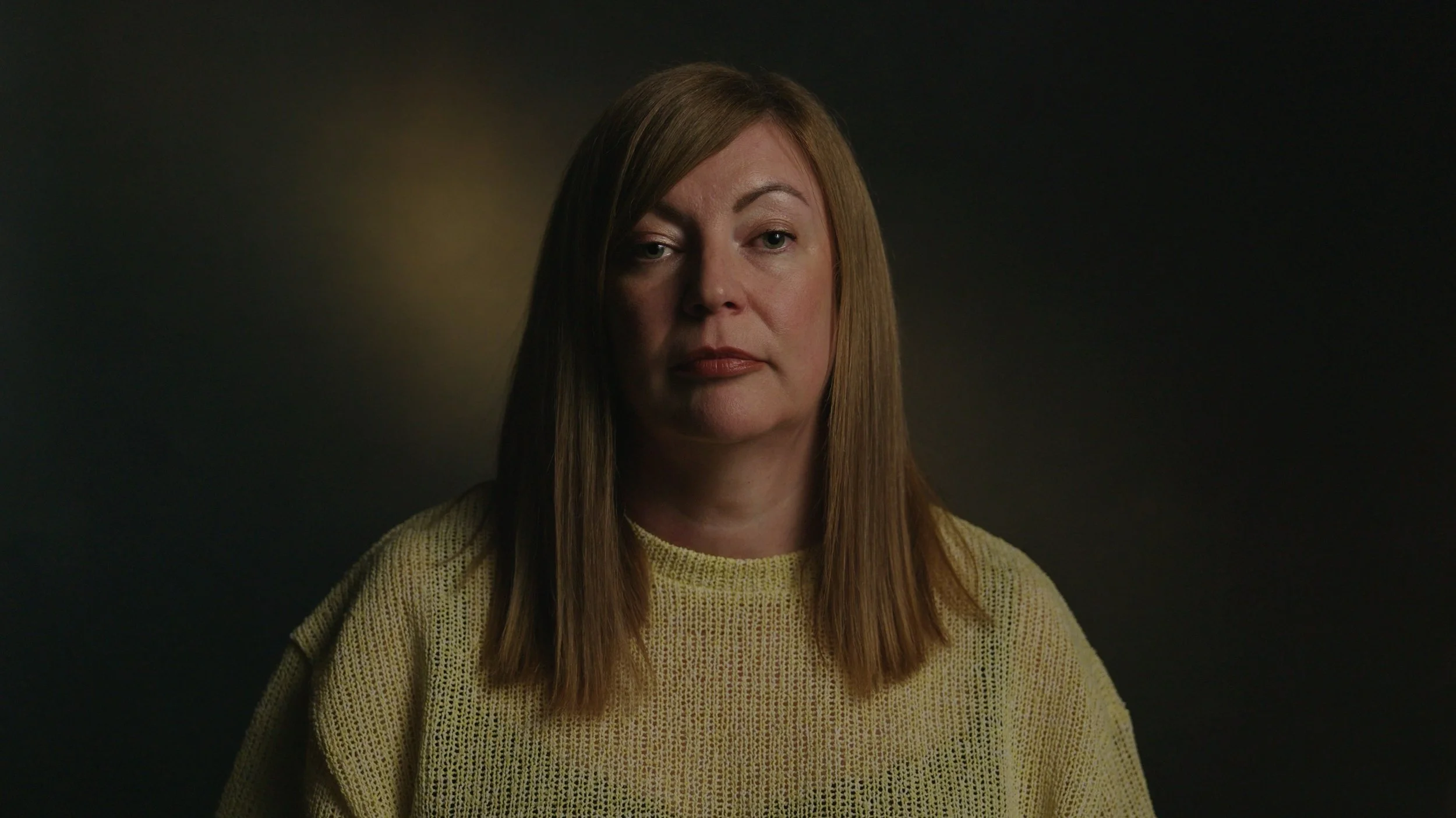 A woman is interviewed in a dark setting with moody lighting