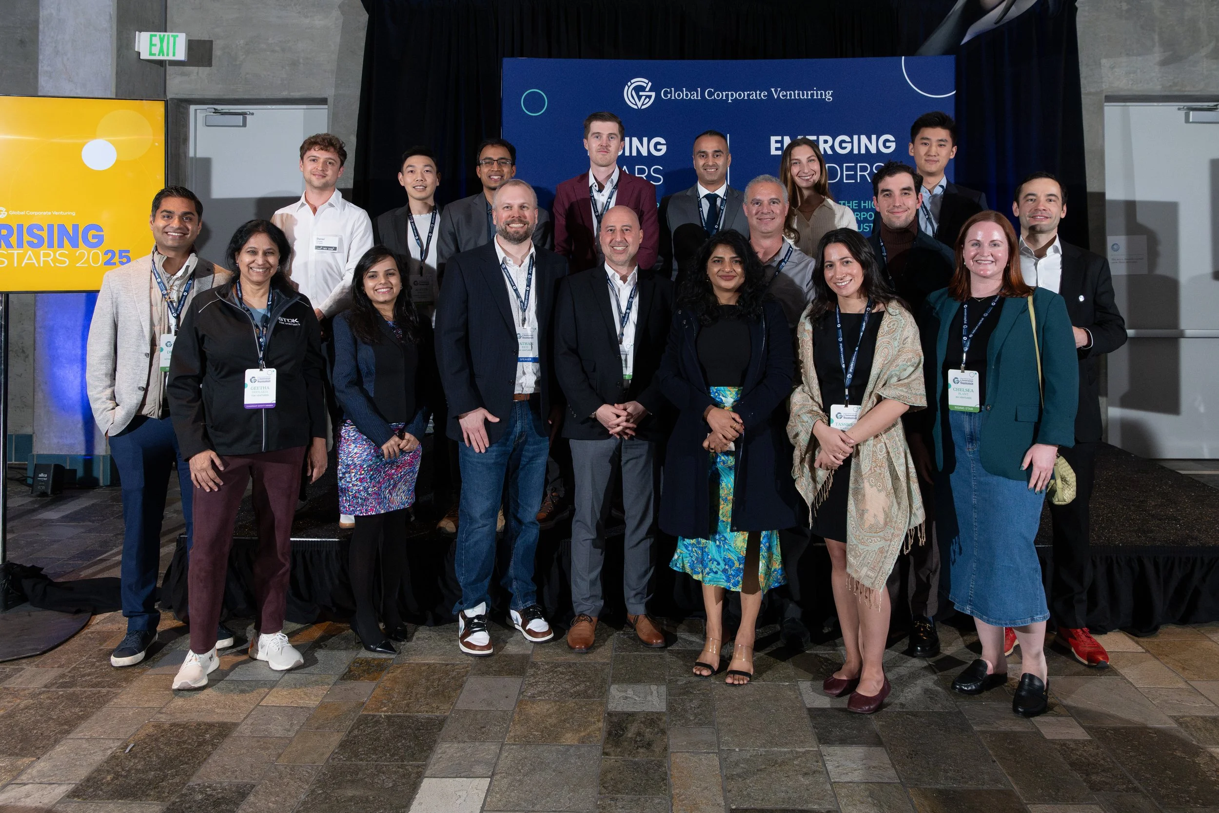 Group of diverse professionals and young adults at a conference or event, standing in front of blue and yellow banners, smiling for the photo.
