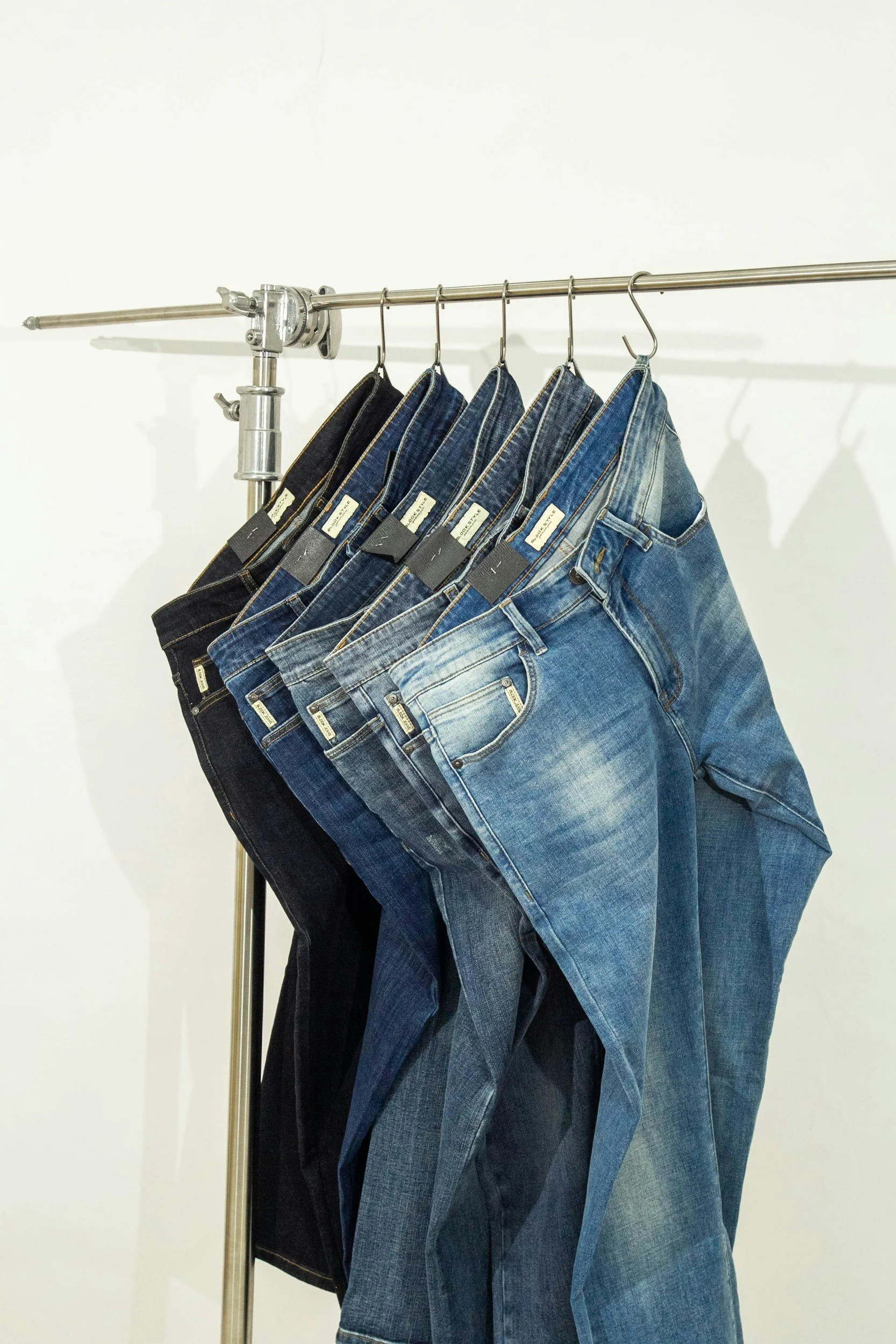Multiple pairs of jeans hanging on a metal clothing rack against a plain white wall