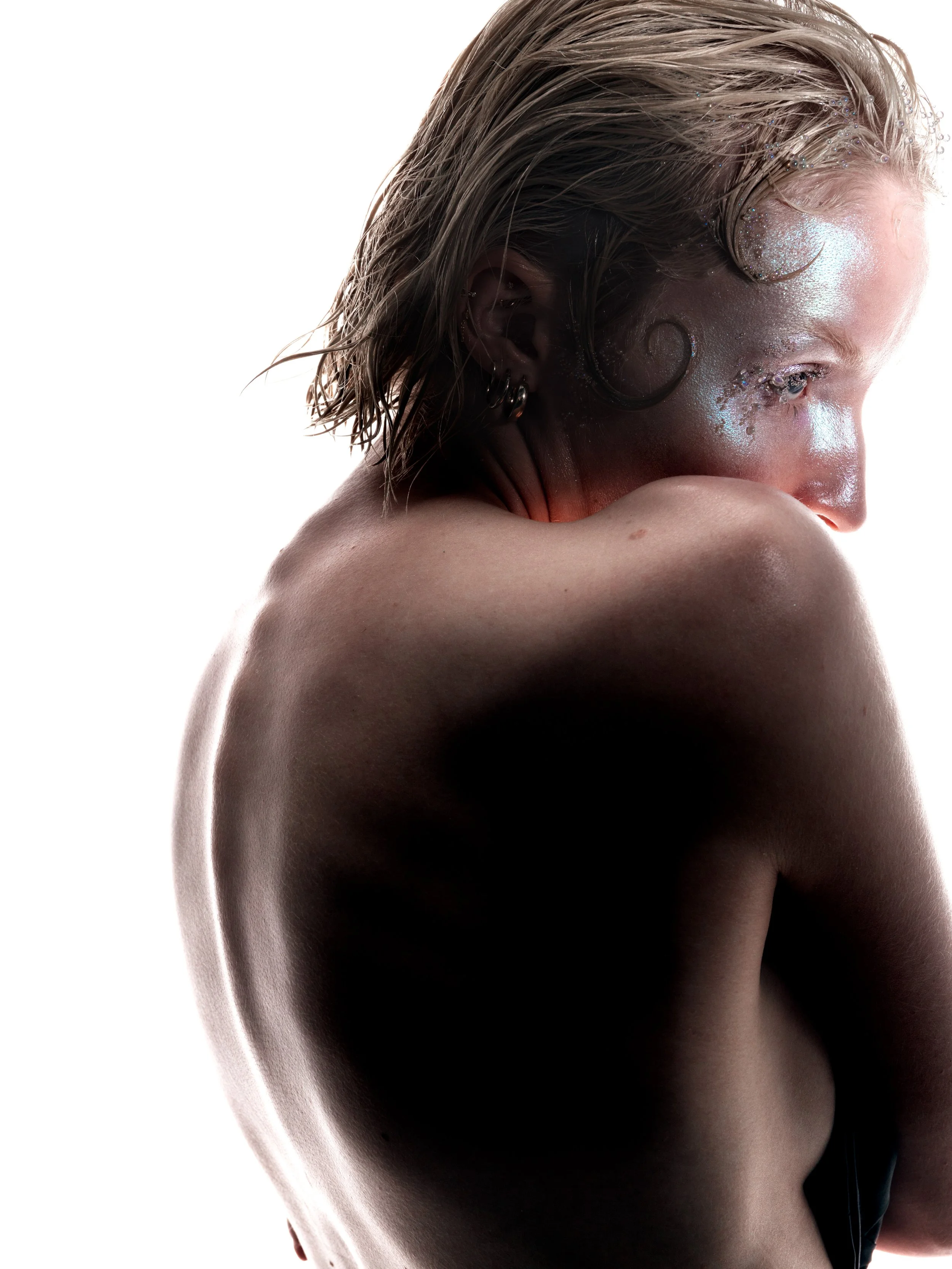 A person with short, wet hair decorated with glitter, looking down with their face resting on their folded arms, against a plain white background.