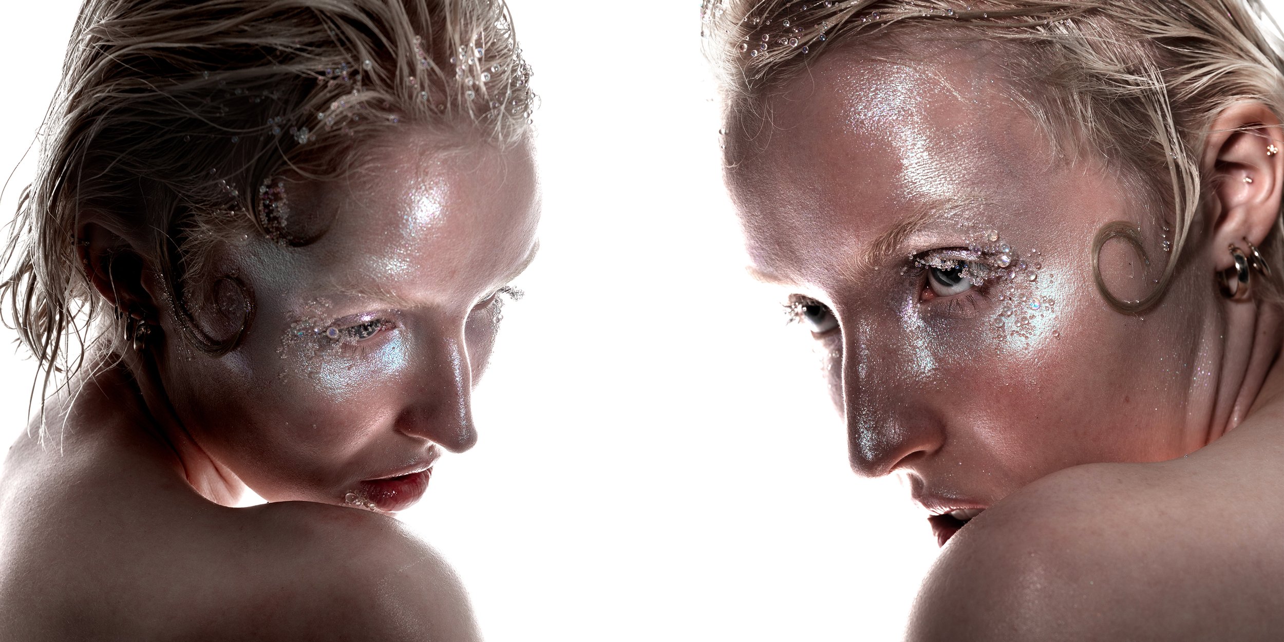 Close-up of two women with platinum blonde hair and glitter makeup, facing each other with contemplative expressions.