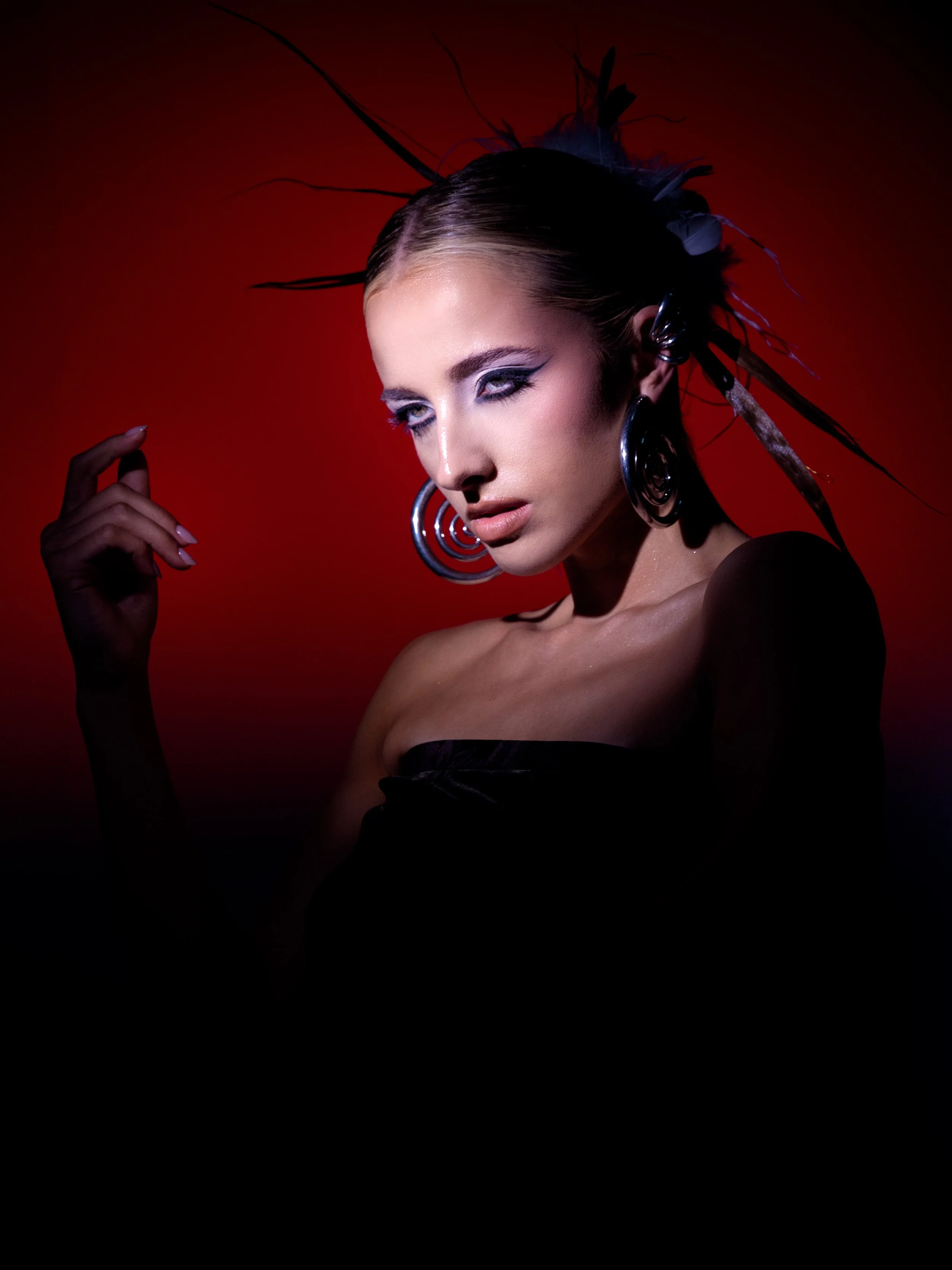A woman with elaborate earrings and feathered headpiece posing against a red background.