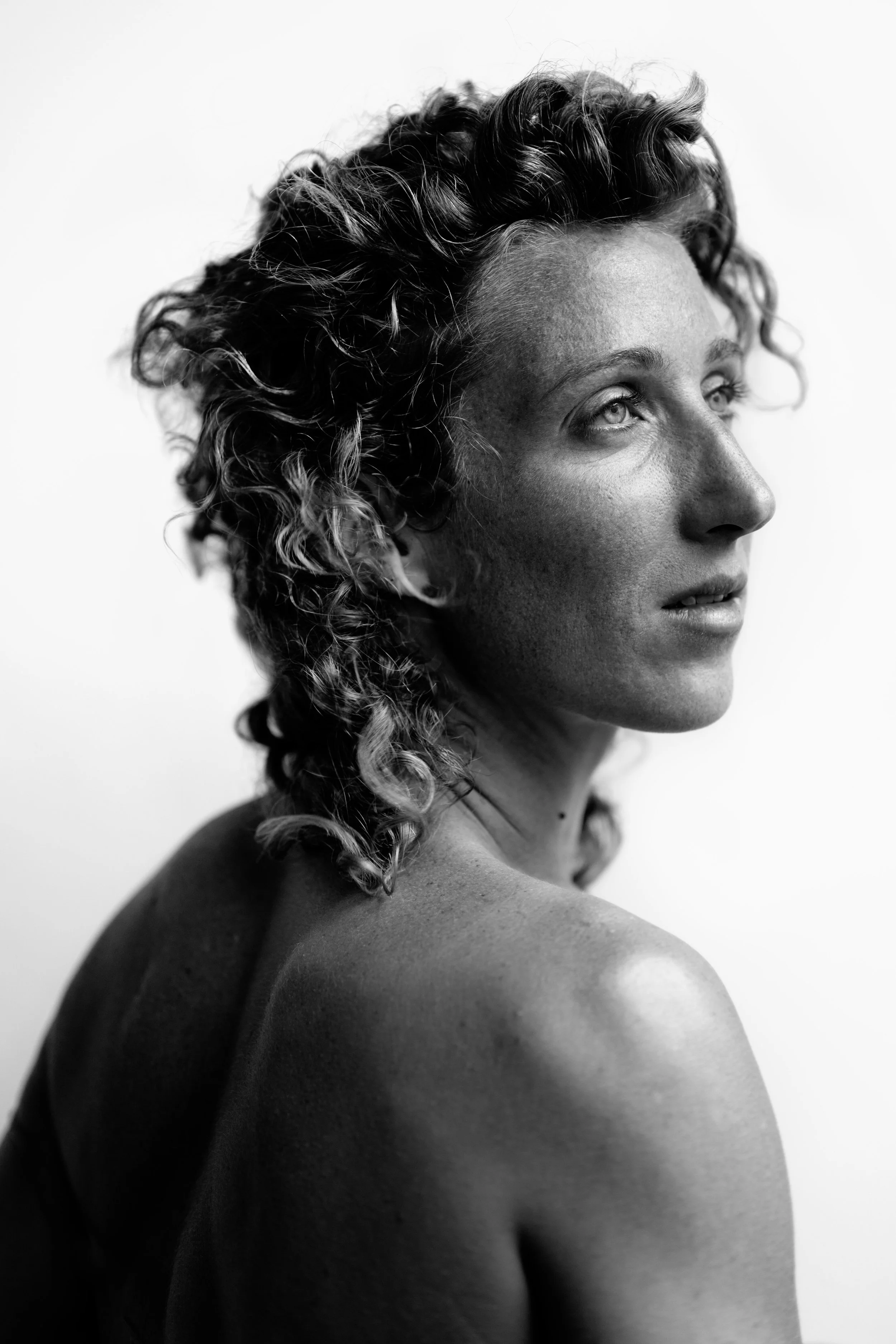 Black-and-white portrait of a woman with curly hair gazing to the side, with visible shoulder and back.